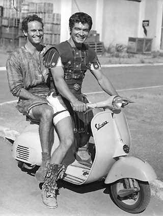 Charlton Heston tooling around in costume on the "Ben-Hur" Cinecitta set at on a Vespa, 1959